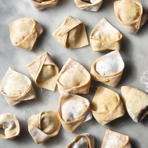 An aerial image of gluten free wontons casually arranged on a white marble table