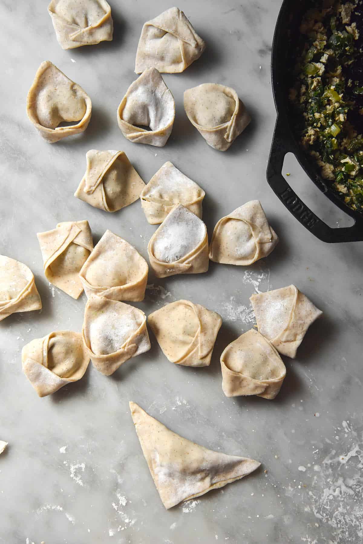 An instructional image demonstrating how to fold gluten free wonton wrappers, set on a white marble table