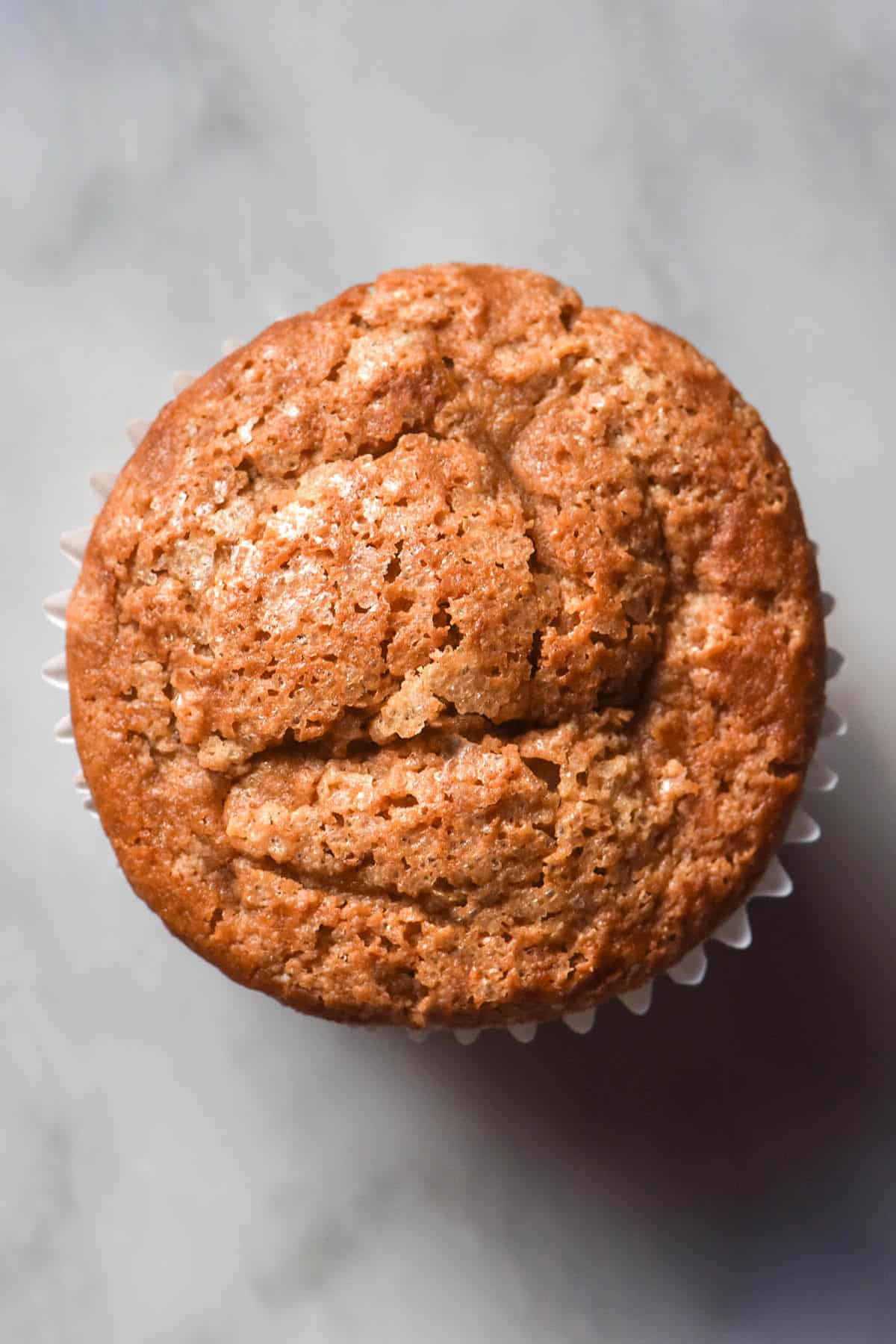 An aerial image of a gluten free buckwheat muffin in a white muffin liner atop a white marble table.