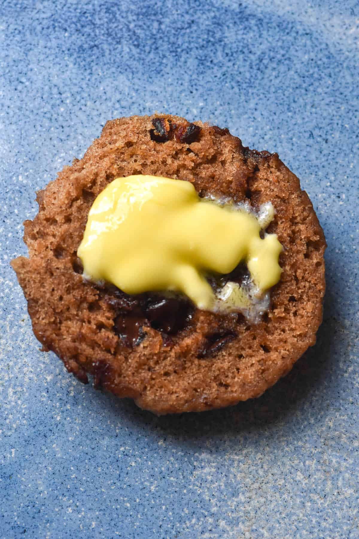 An aerial image of a piece of gluten free hot cross bun topped with melting butter. 