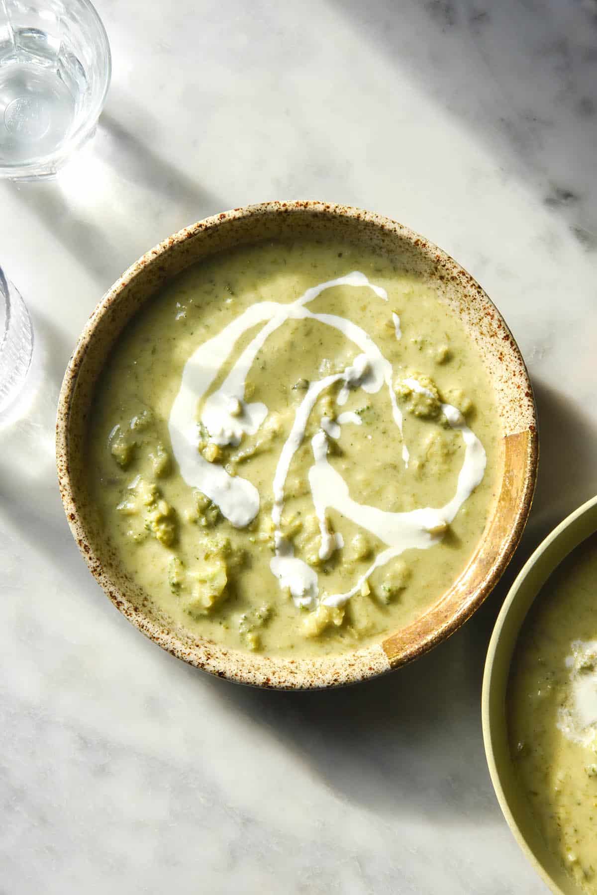A sunlit aerial image of a bowl of low FODMAP broccoli cheddar soup on a white marble table