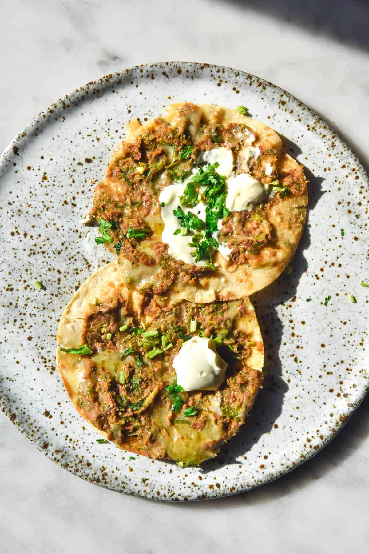 A brightly lit aerial image of two corn tortillas topped with low FODMAP refried beans, melted cheddar, sour creams and coriander. 