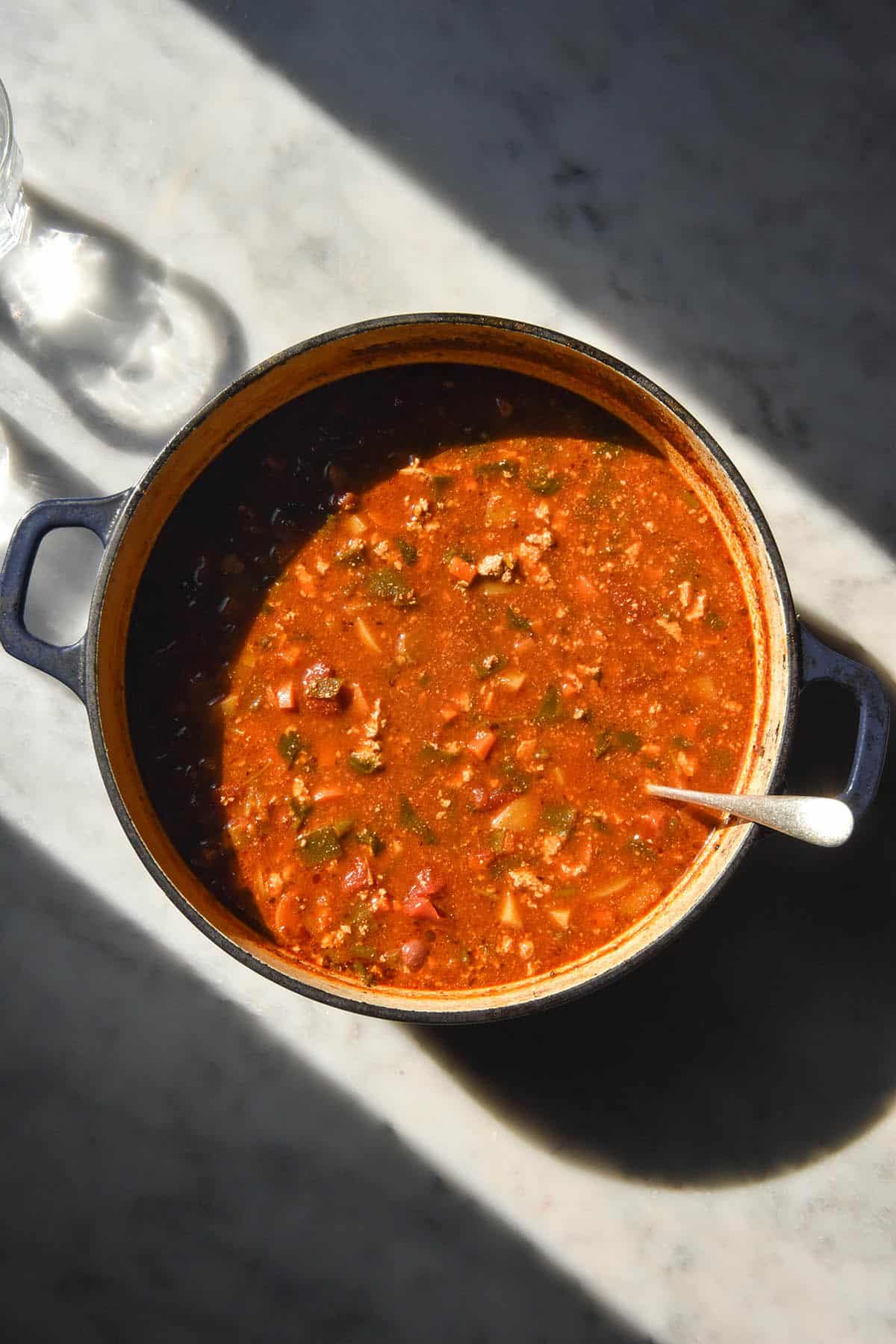 An aerial image of a pot of vegetarian taco soup on a white marble table in contrasting sunlight. 