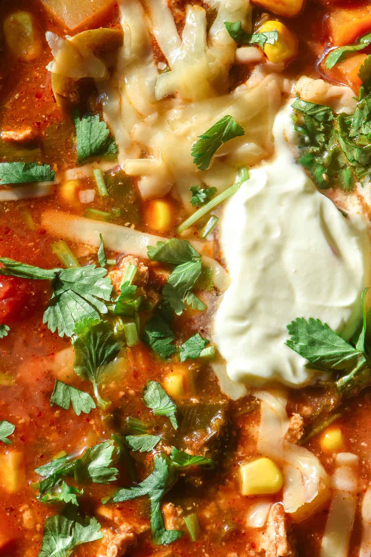 A close up aerial macro image of a bowl of vegetarian taco soup topped with sour cream, melting cheese and coriander.
