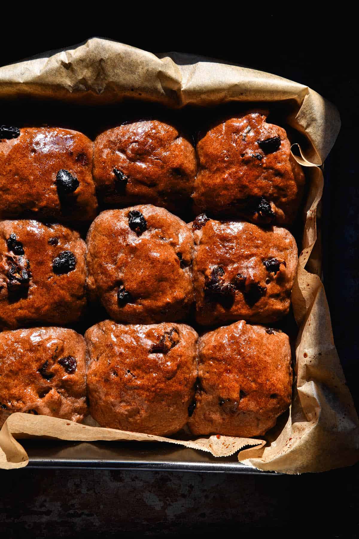 An aerial image of a tray of gluten free hot cross buns without yeast in bright sunlight against a dark backdrop