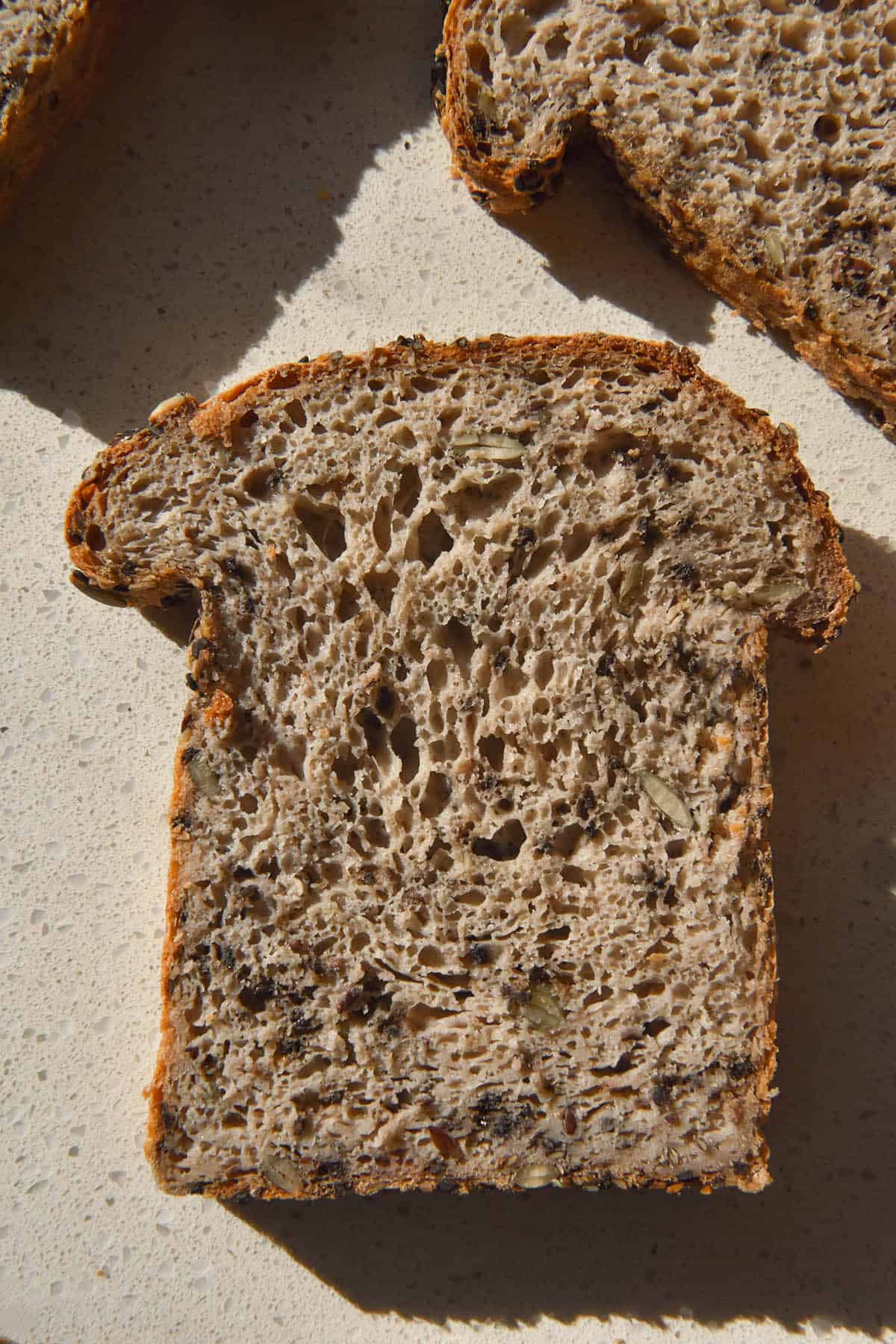 An aerial image of slices of gluten free seeded bread on a white stone bench top in bright sunlight.