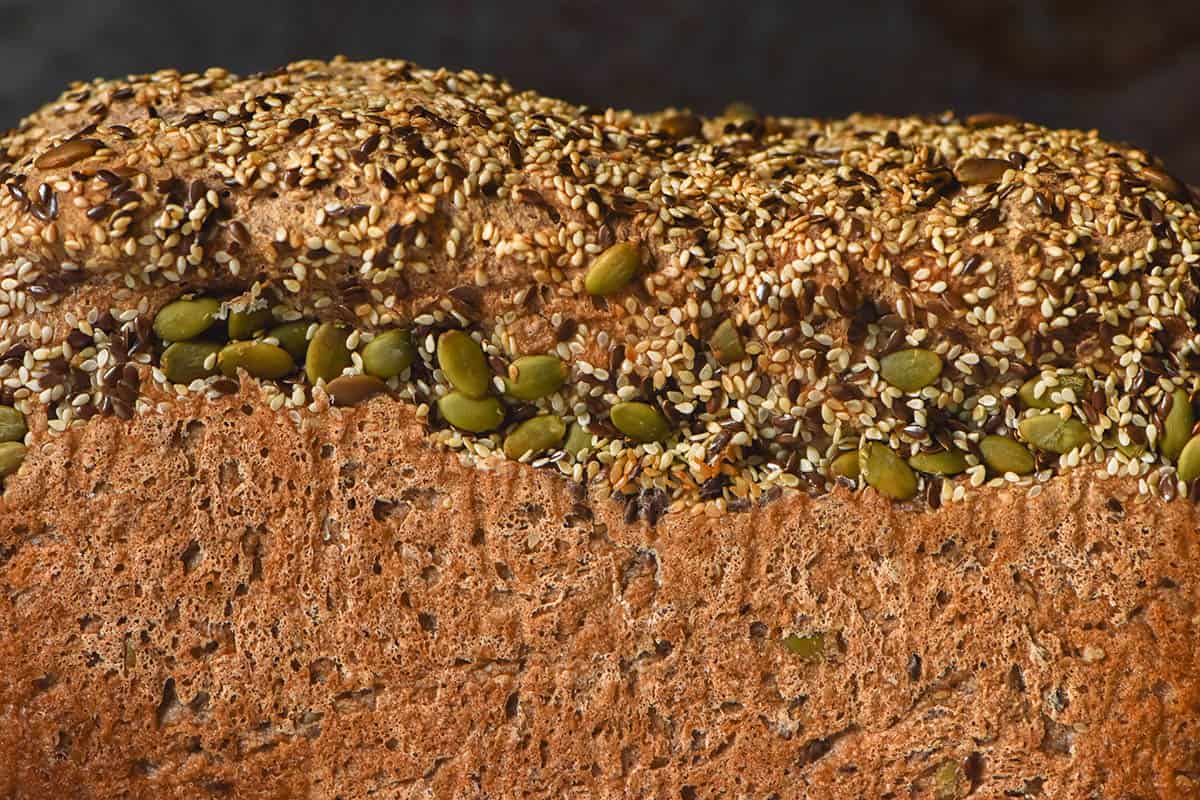 A side on image of a loaf of gluten free seeded bread. The loaf is golden brown and topped with plenty of seeds which have embedded into the side of the loaf.