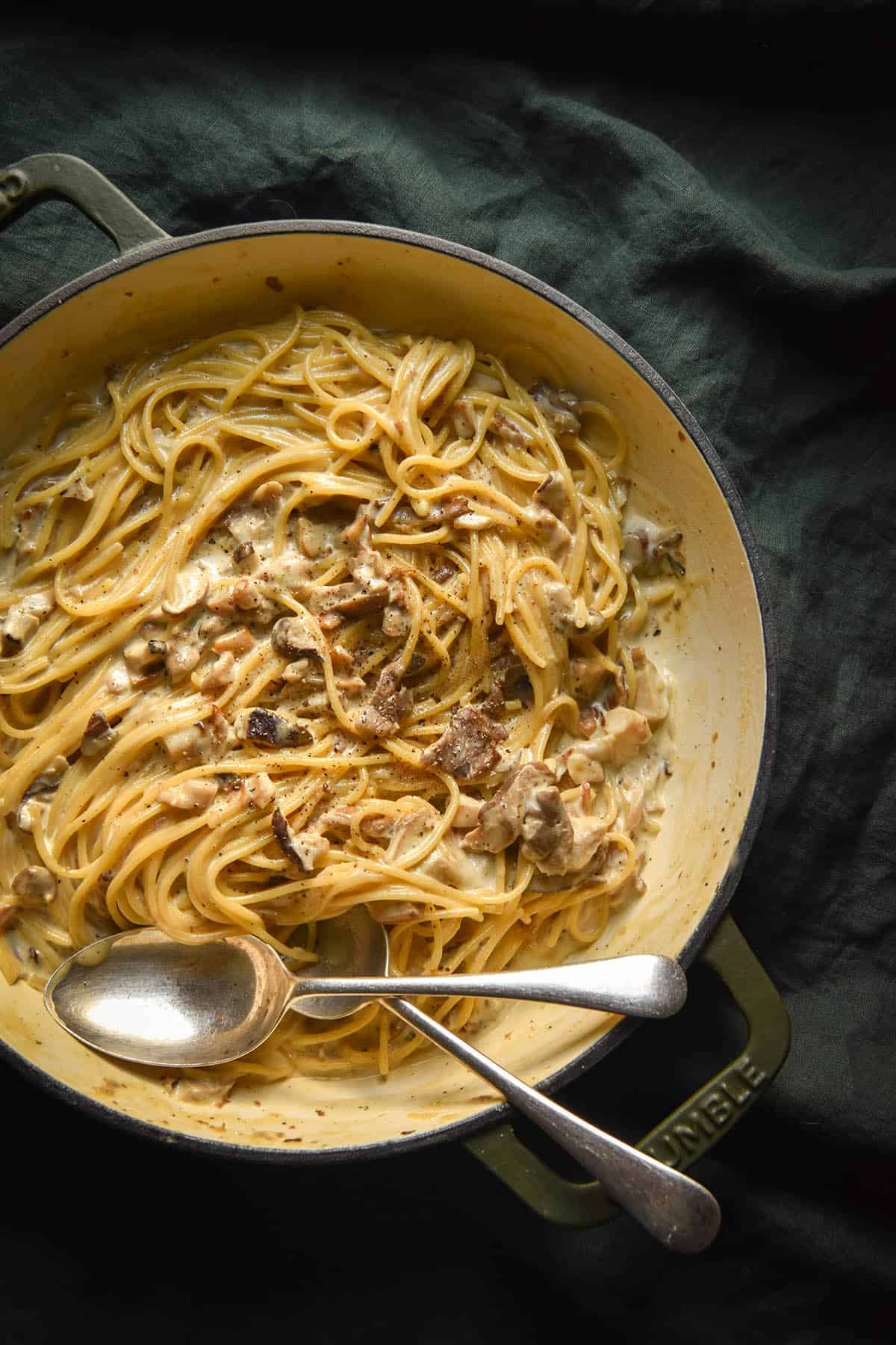 An aerial image of a skillet filled with low FODMAP creamy mushroom pasta on a dark olive linen tablecloth.