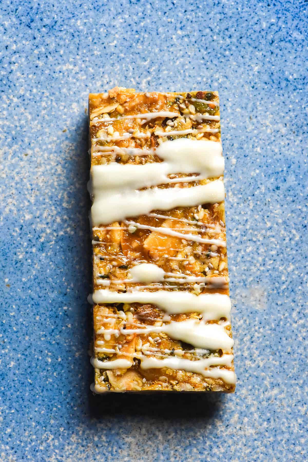 An aerial image of a gluten free granola bar drizzled with white chocolate atop a bright blue ceramic plate