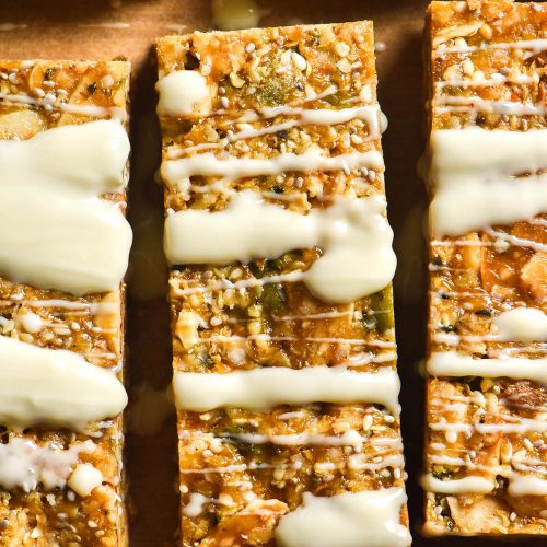 An aerial close up image of gluten free granola bars on brown baking paper that have been drizzled with white chocolate