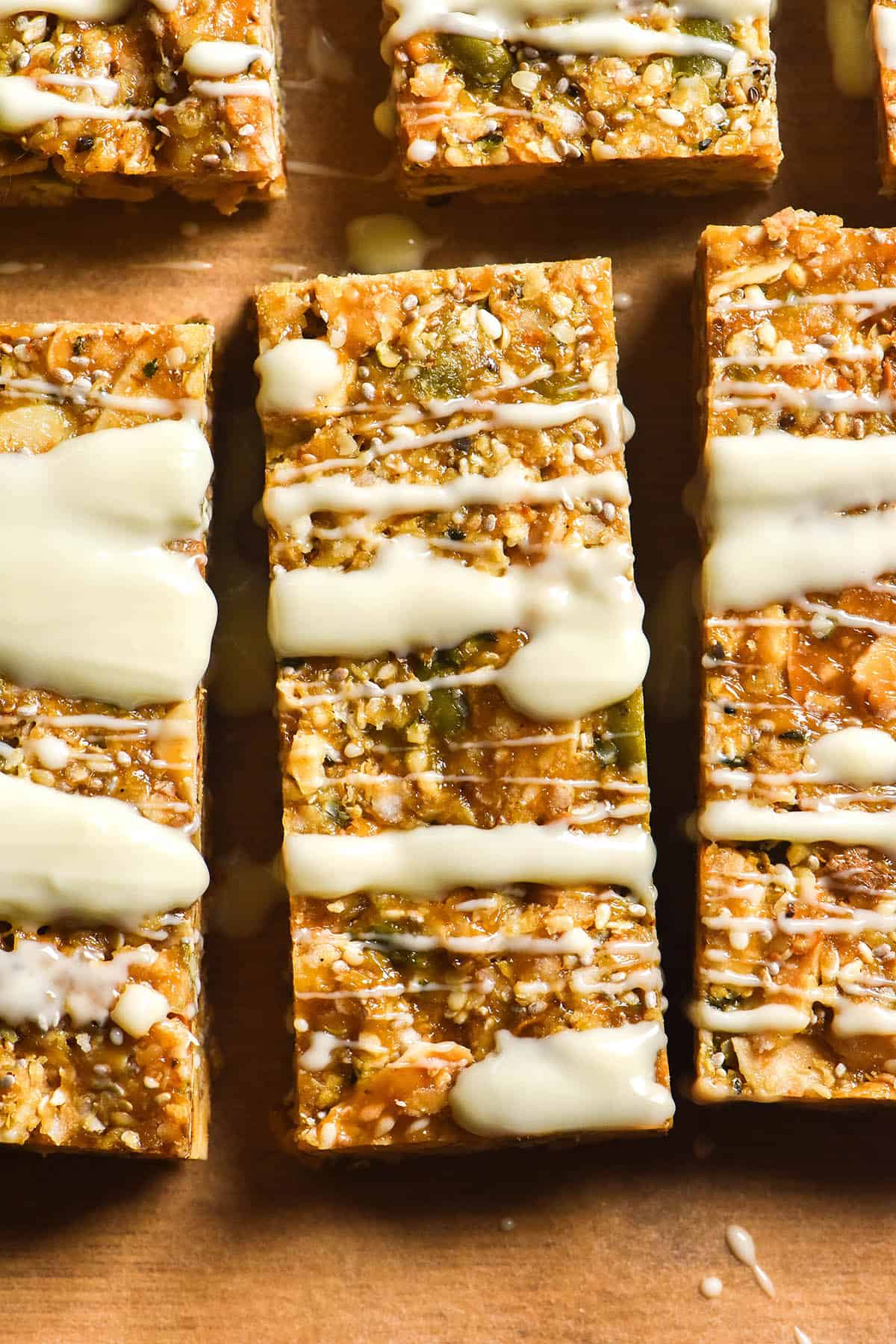An aerial close up image of gluten free granola bars on brown baking paper that have been drizzled with white chocolate