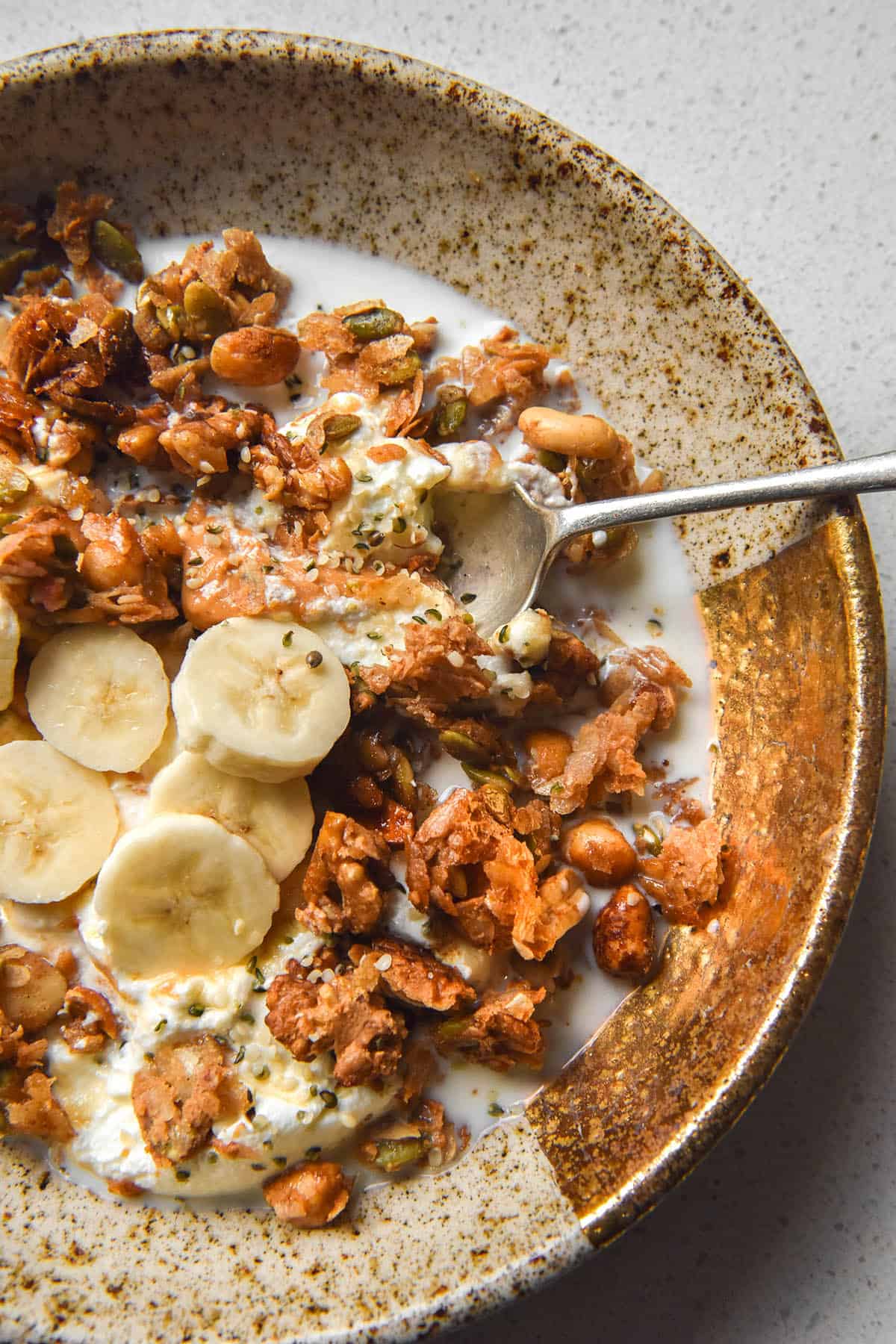 An aerial image of a bowl of low FODMAP granola with milk, bananas and yoghurt on a white marble table