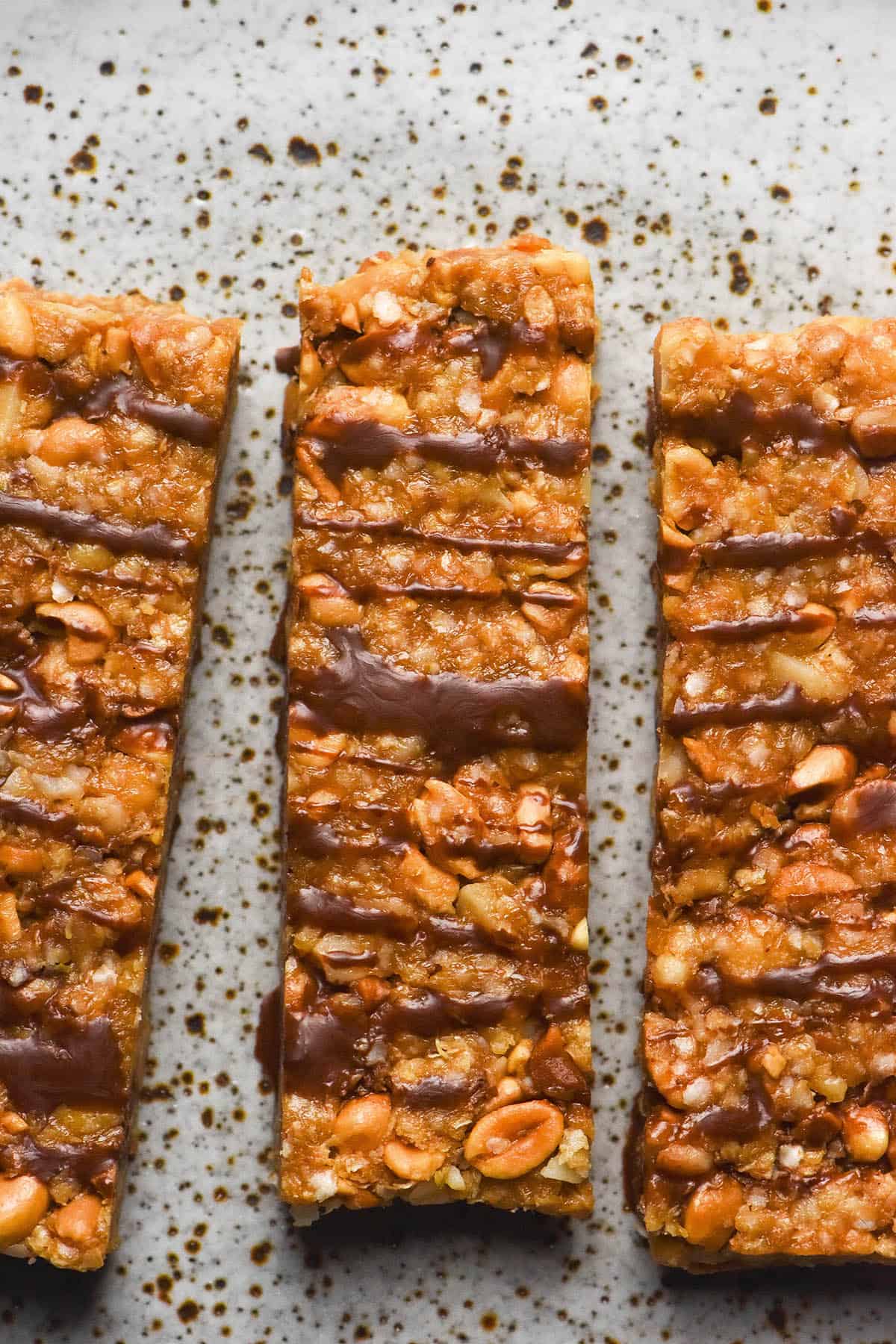 An aerial sunlit image of Low FODMAP granola bars drizzled with chocolate and sitting on a white speckled ceramic plate.