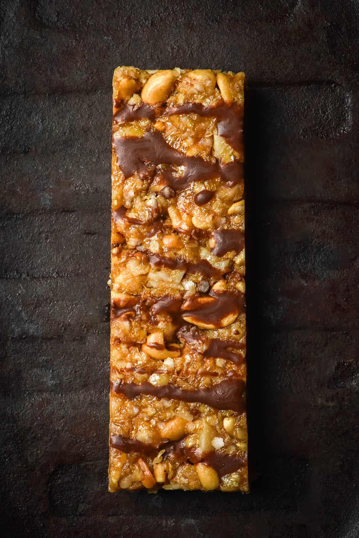 An aerial image of a Low FODMAP granola bar drizzled with chocolate on a dark steel plate
