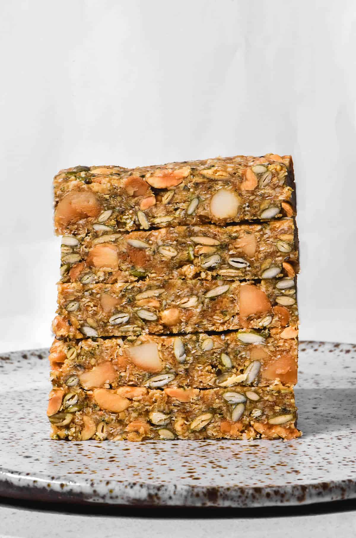 A brightly lit aerial image of a stack of low FODMAP granola bars on a white speckled ceramic plate against a white backdrop