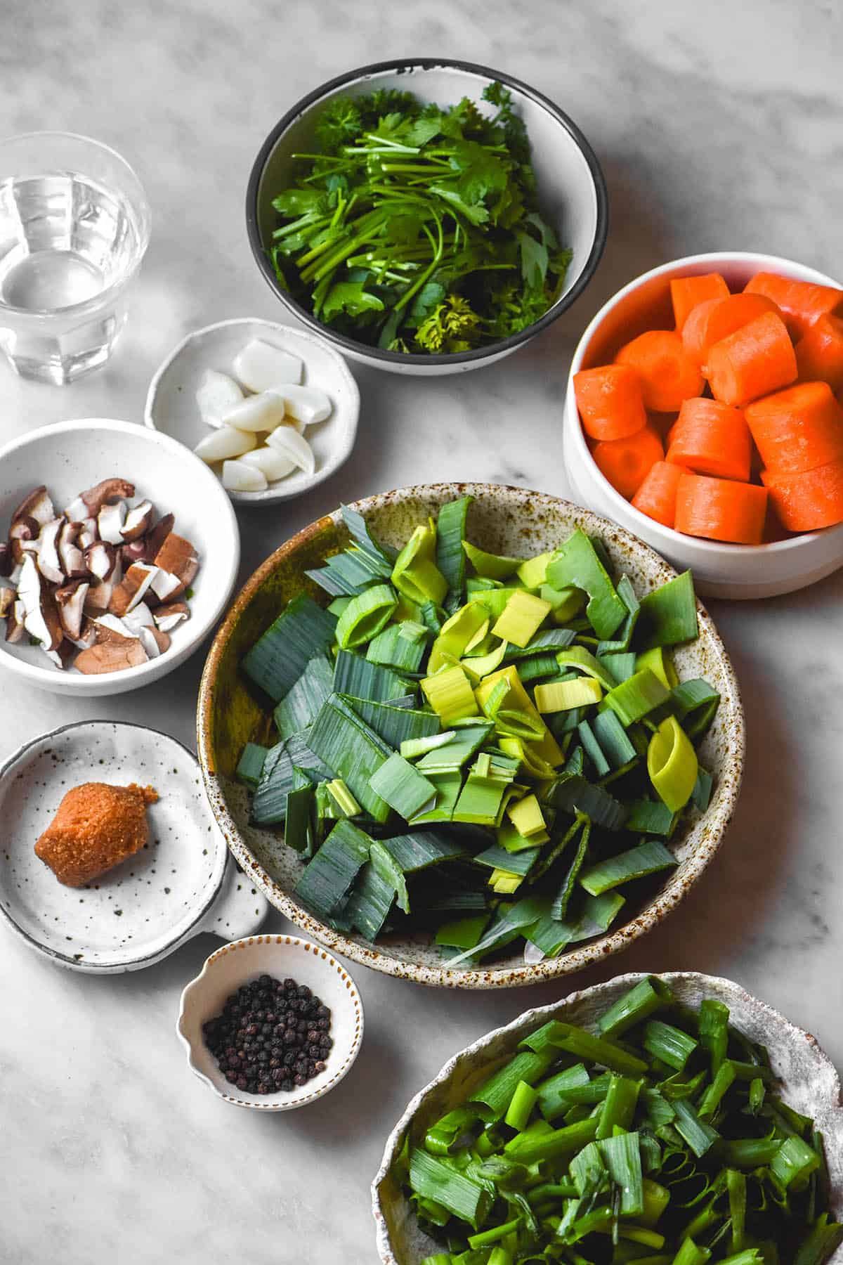 An aerial image of the ingredients to make a low FODMAP vegetable stock arranged in various sized bowls on a white marble table