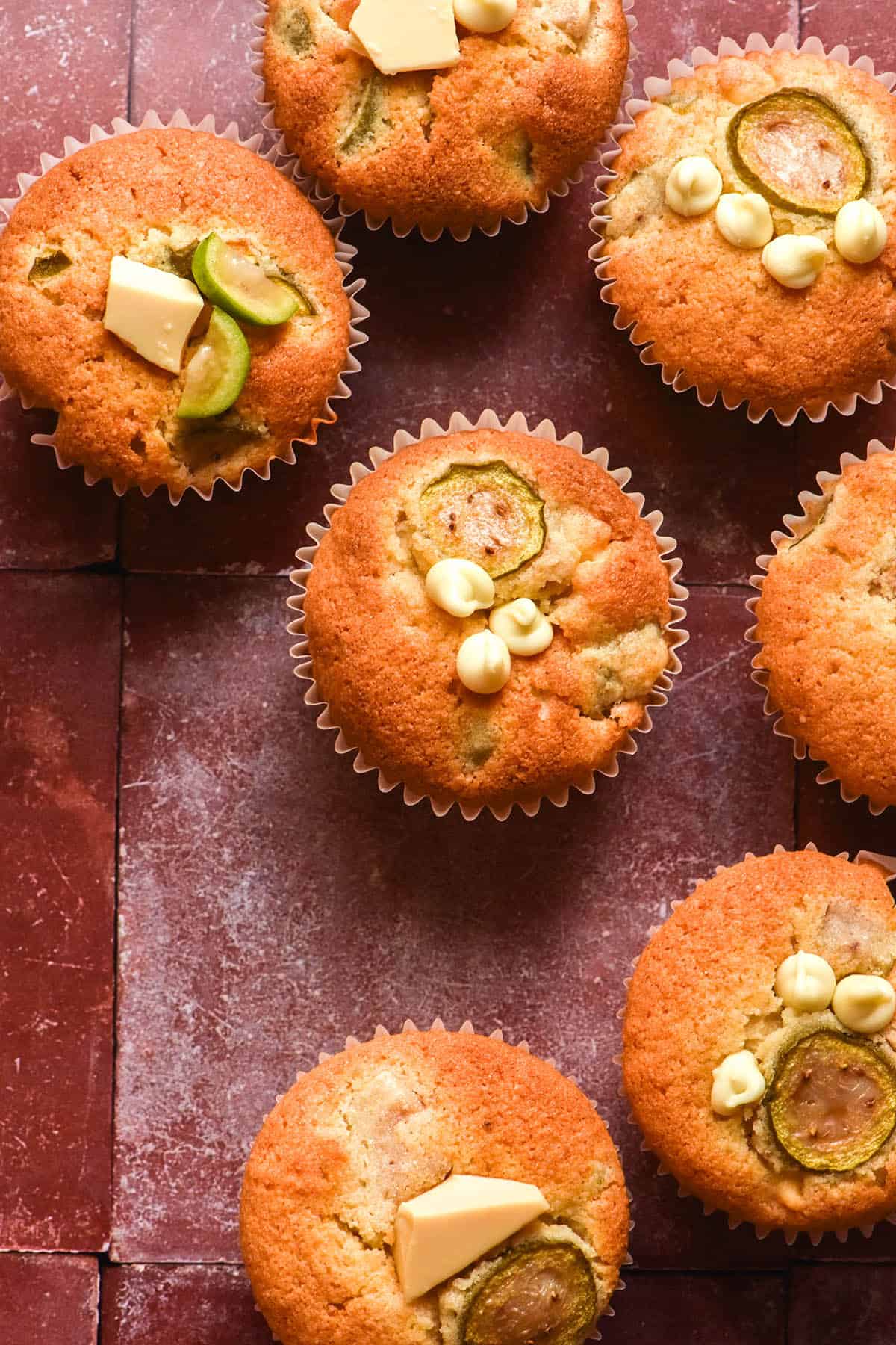 An aerial image of gluten free feijoa and white chocolate muffins atop a terracotta tile backdrop