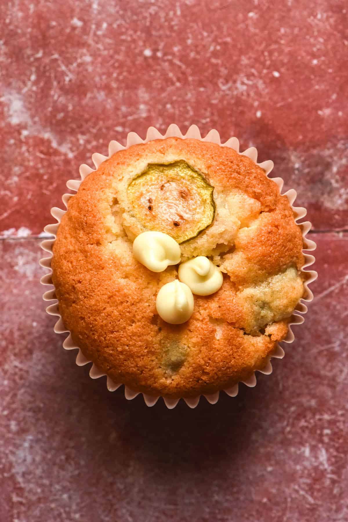 An aerial image of a gluten free feijoa and white chocolate muffin atop a terracotta tile backdrop