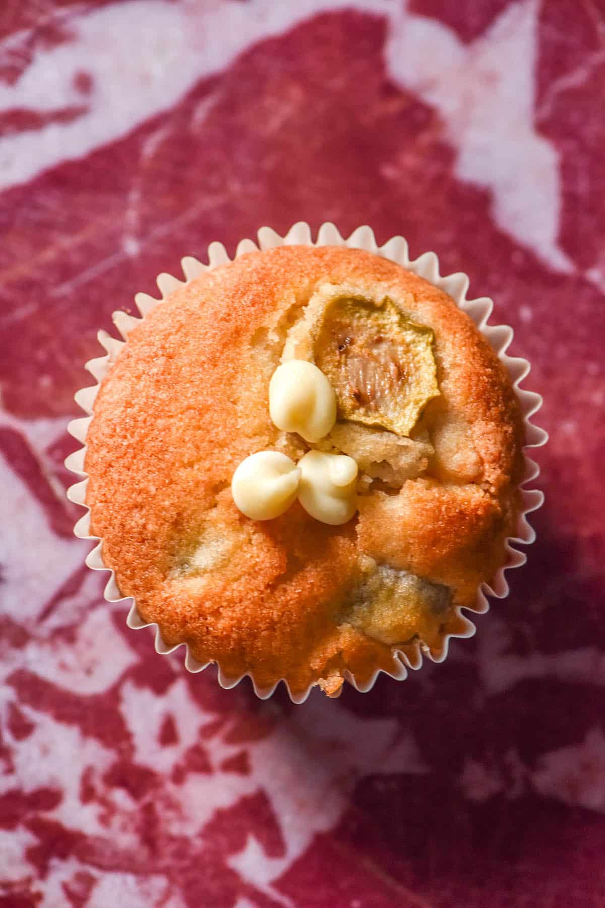An aerial image of a gluten free feijoa and white chocolate muffin atop a mauve and white marbled backdrop