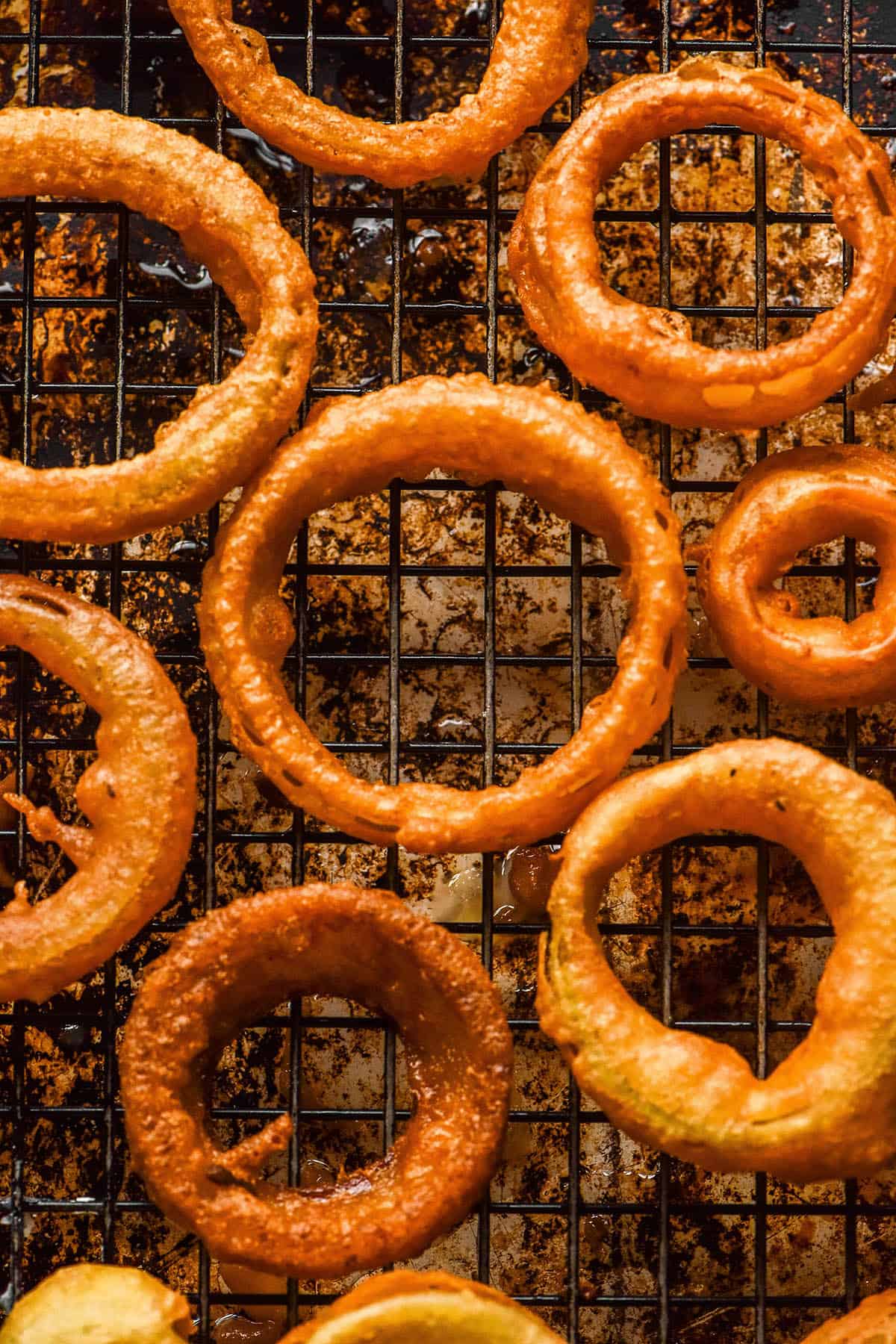 An aerial image of gluten free onion rings on a cooling rack atop a dark mottled baking tray