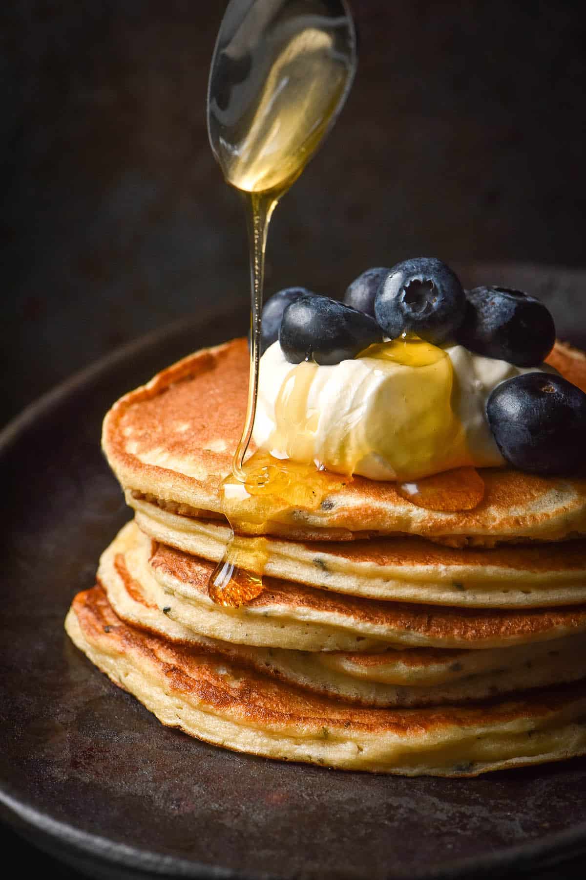 A side on image of gluten free protein pancakes stacked and topped with yoghurt, blueberries and a drizzle of honey