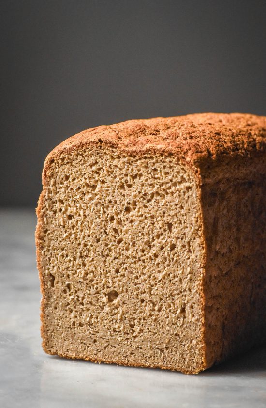 A moody side on image of a loaf of teff bread on a white marble table against a dark backdrop. The bread has been sliced, revealing the soft crumb inside.