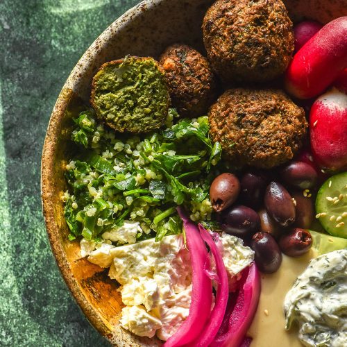 An aerial image of a low FODMAP falafel bowl atop a bright green sunlit backdrop.