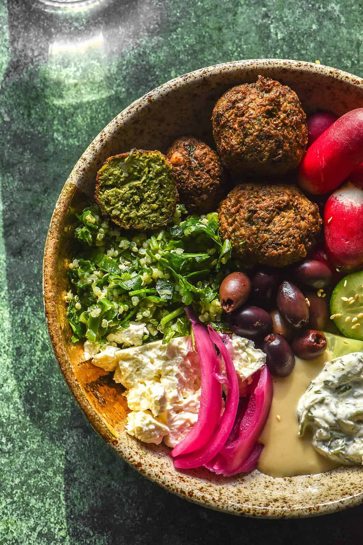 A brightly lit aerial image of a low FODMAP falafel bowl on an olive green backdrop