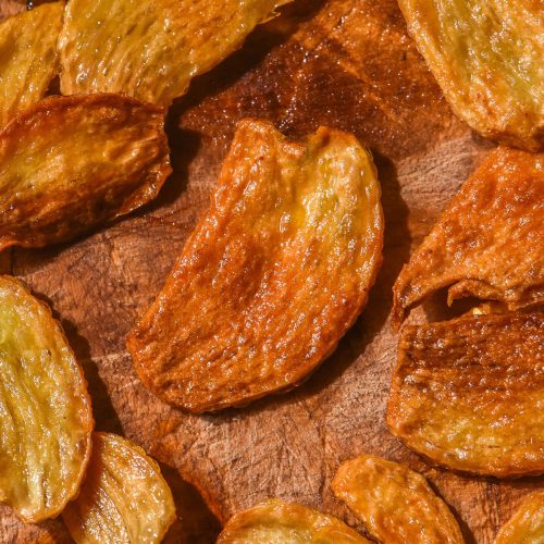 A brightly lit aerial image of golden brown low FODMAP garlic chips on a wooden backdrop