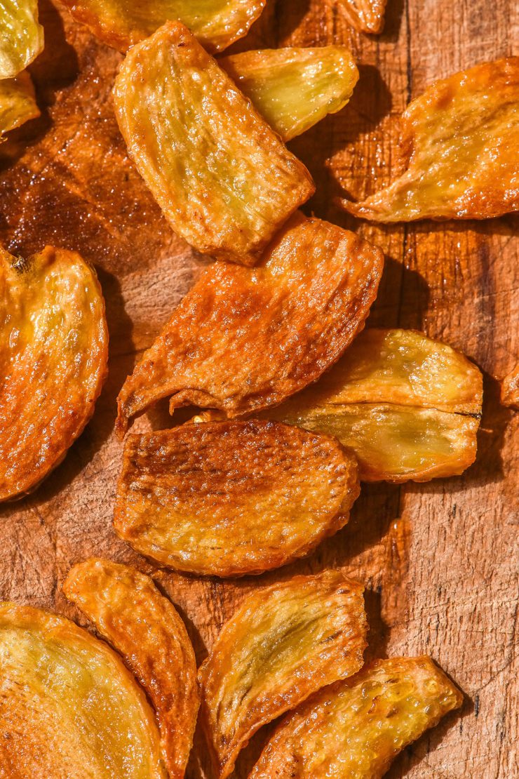 A brightly lit aerial image of golden brown crispy low FODMAP garlic chips made using pickled garlic. The garlic chips sit on a medium wooden backdrop