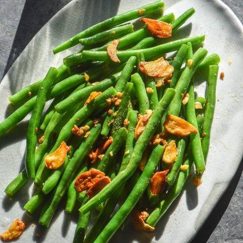 An aerial image of low FODMAP garlic green beans on a white oval table atop a dark blue backdrop
