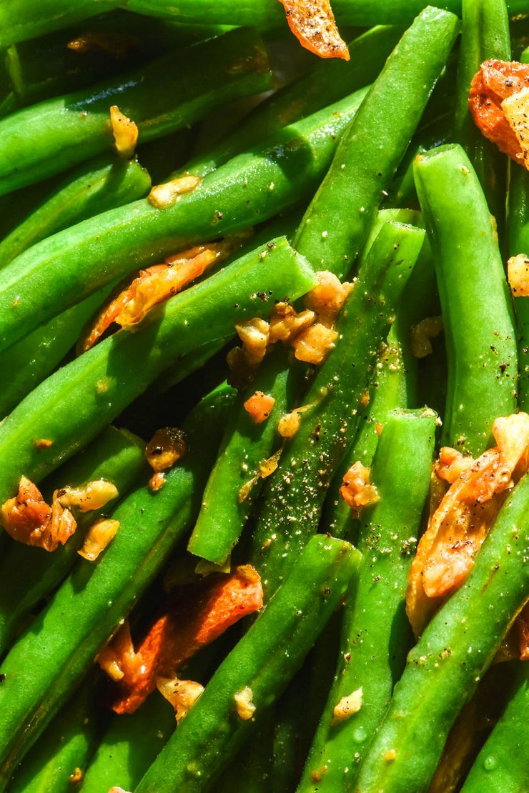 An aerial brightly lit image of low FODMAP garlic green beans topped with low FODMAP garlic chips, salt and pepper