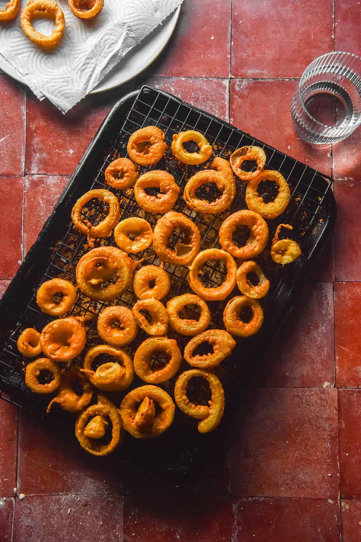 An aerial image of low FODMAP onion rings on a cooling track atop a baking tray. The baking tray sits on a terracotta tile backdrop