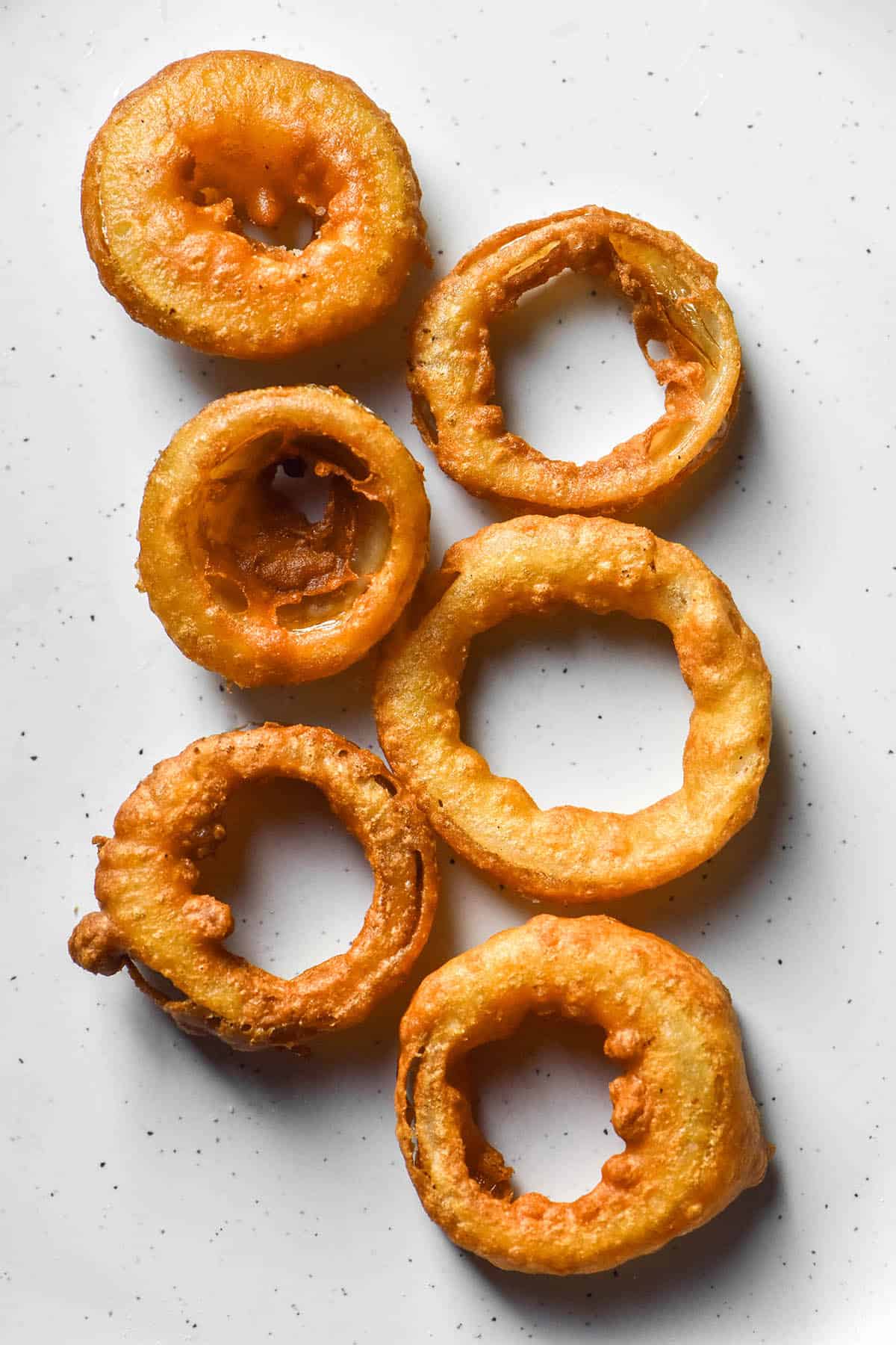 An aerial image of 6 low FODMAP onion rings on a white plate