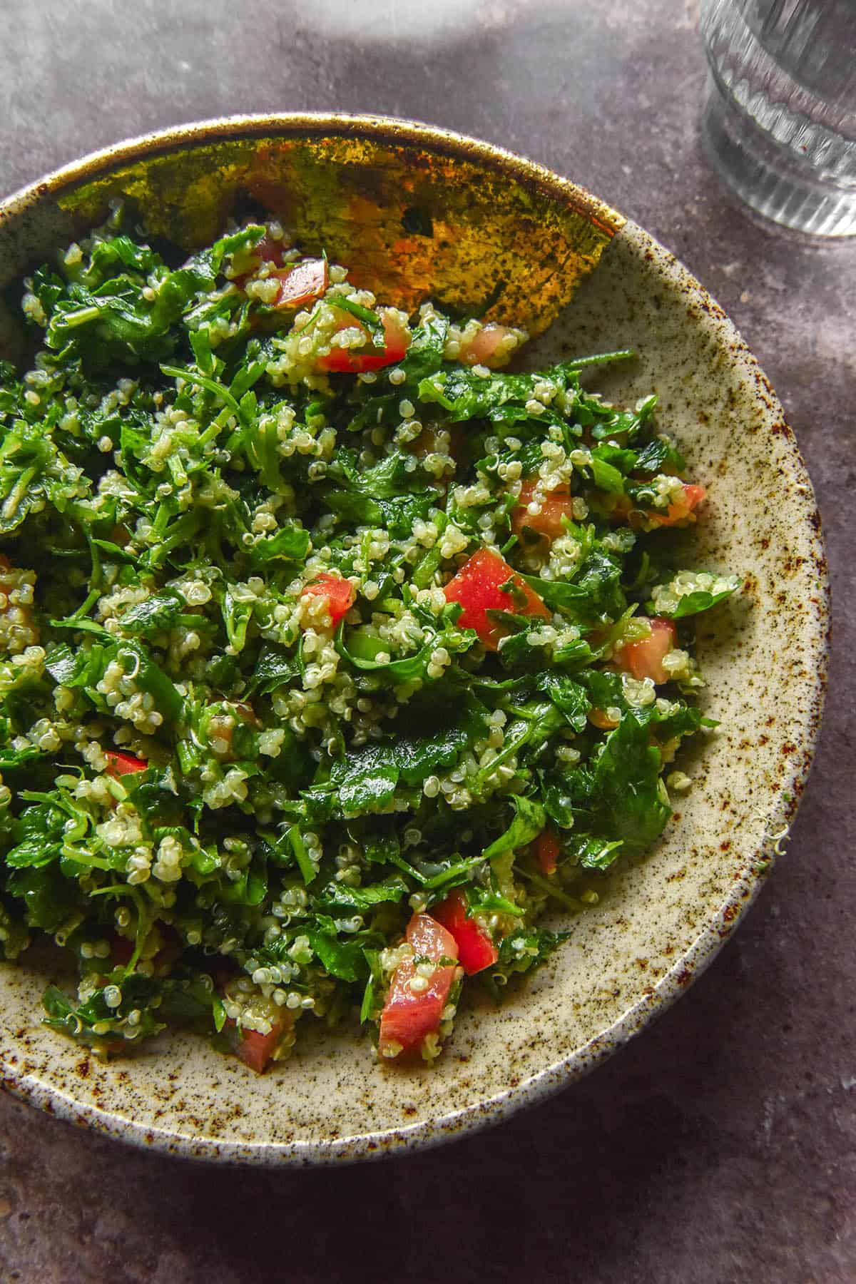 An aerial image of a speckled ceramic bowl filled with low FODMAP tabbouleh on a medium grey backdrop