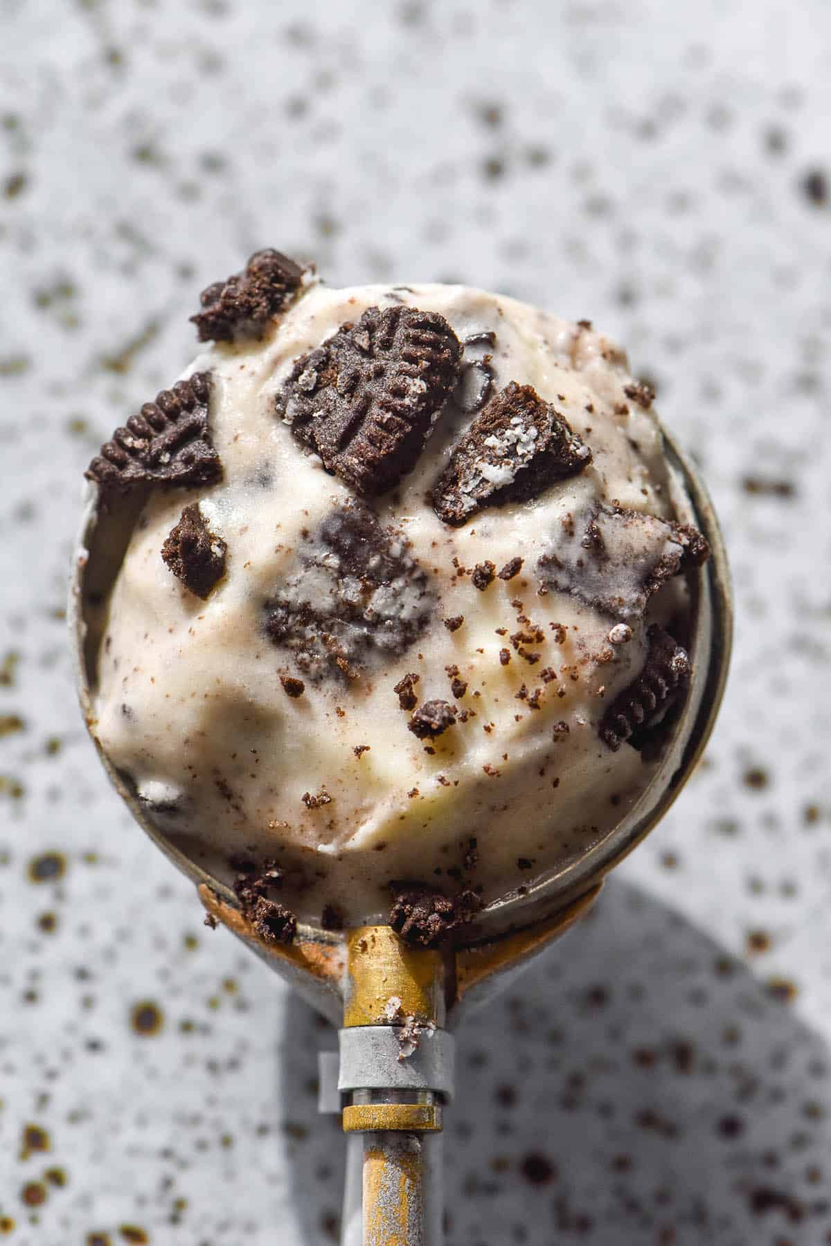 An aerial close up image of a scoop of cookies and cream ice cream atop a white speckled ceramic plate