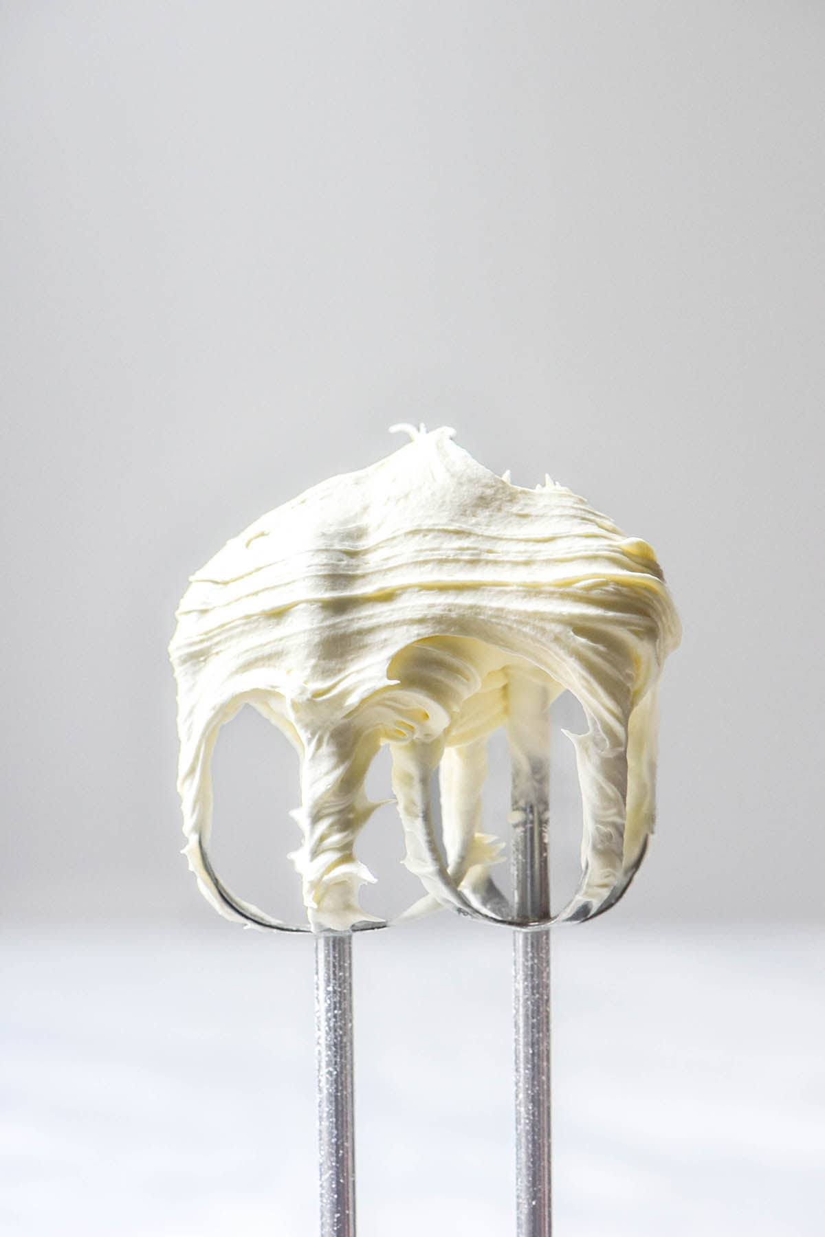 A side on image of two hand beaters filled with whipped cream against a white backdrop