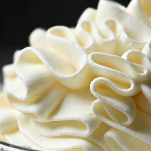 A side on macro image of lactose free whipping cream piped into a small white ceramic bowl against a dark backdrop