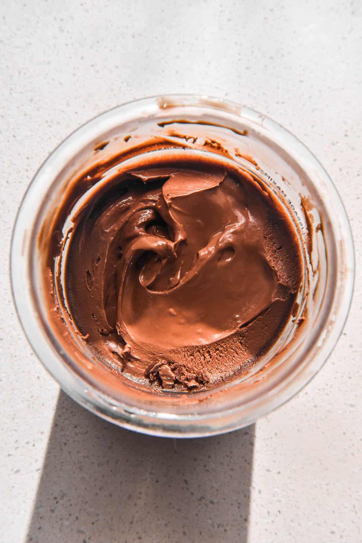 An aerial image of a tub of Ninja Creami chocolate ice cream on a white stone bench top