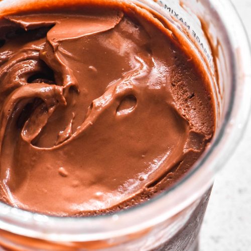 A close up macro image of tub of Ninja Creami chocolate ice cream on a white stone bench top