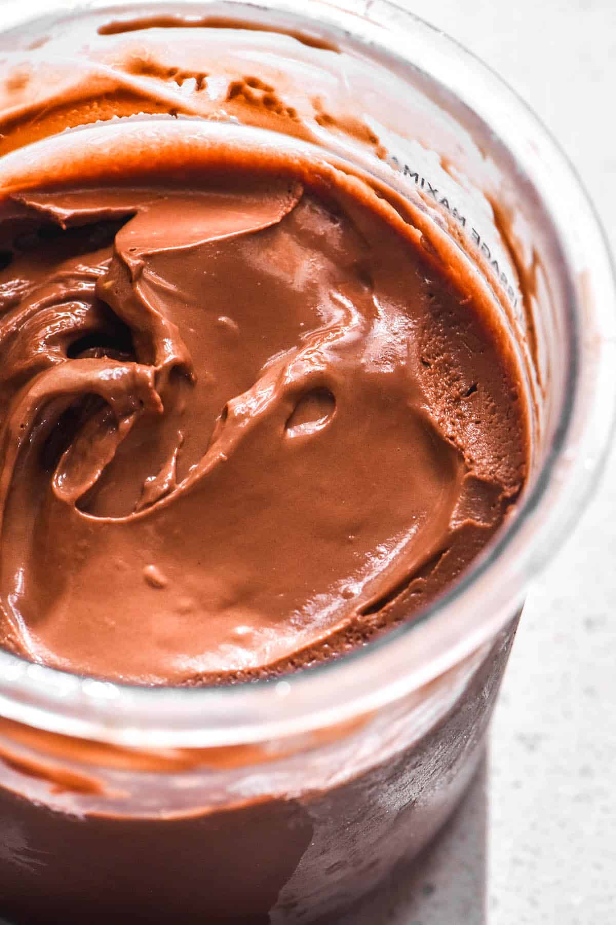 A close up macro image of tub of Ninja Creami chocolate ice cream on a white stone bench top