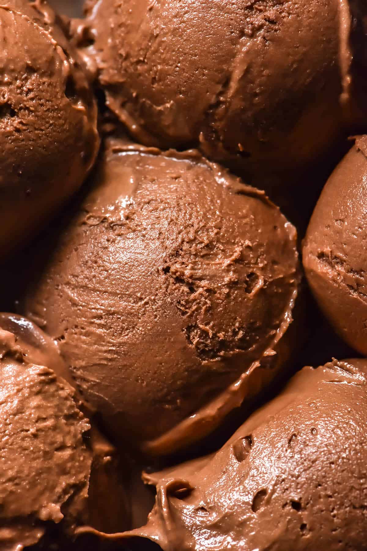 An aerial macro image of six scoops of chocolate ice cream sitting snugly in a dark ceramic bowl