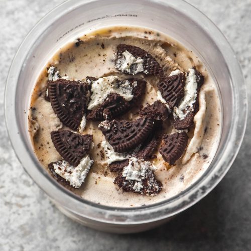 An aerial image of a tub of Ninja Creami cookies and cream ice cream topped with extra gluten free Oreos on a light grey steel backdrop