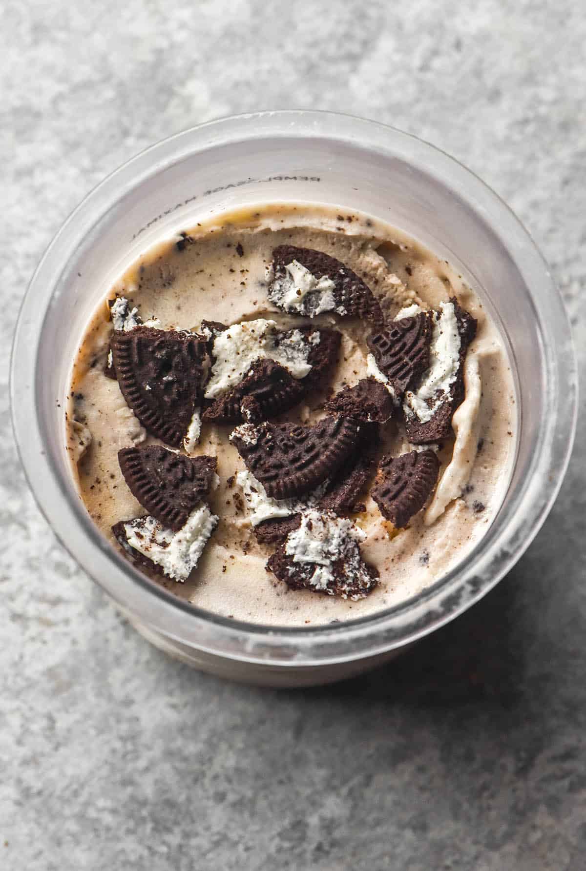 An aerial image of a tub of Ninja Creami cookies and cream ice cream topped with extra gluten free Oreos on a light grey steel backdrop