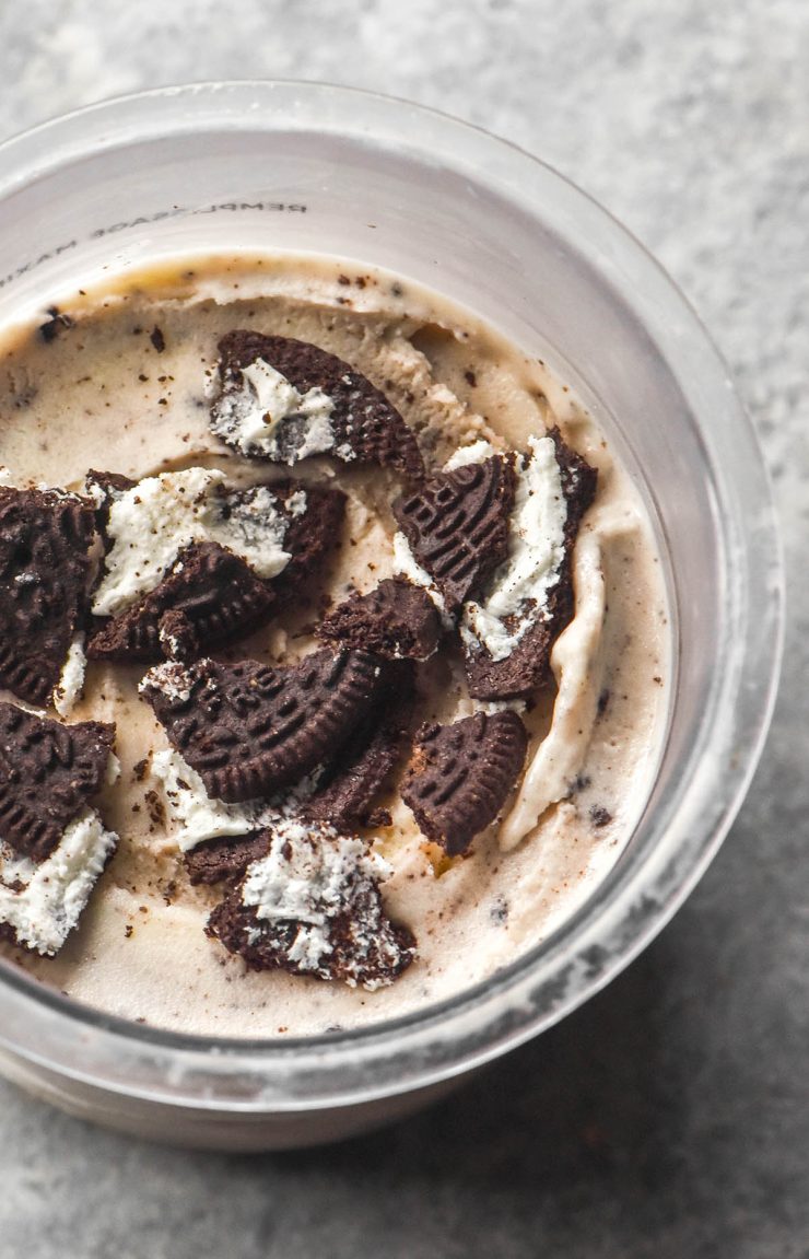 An aerial image of a tub of Ninja Creami cookies and cream ice cream topped with extra gluten free Oreos on a light grey steel backdrop