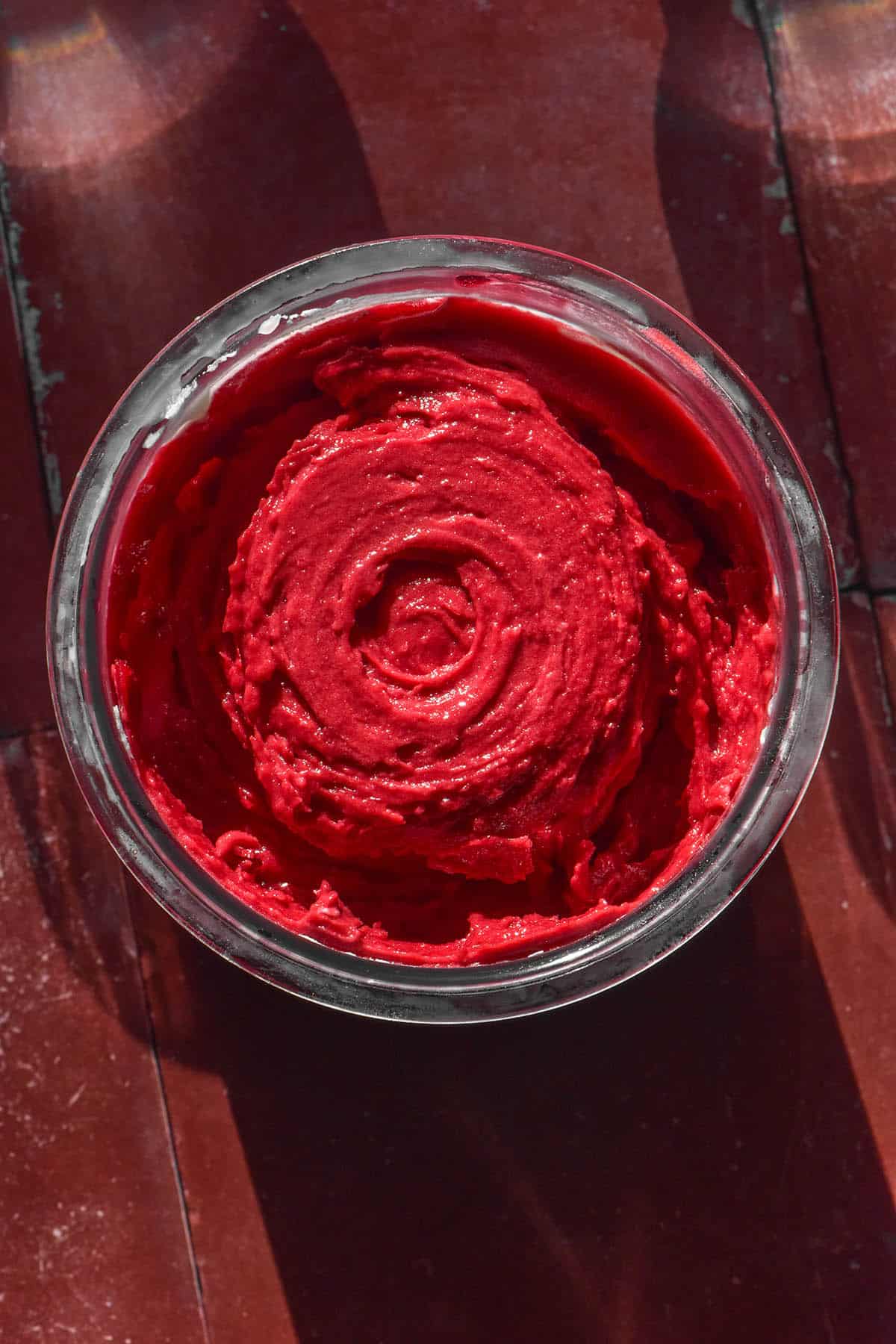 An aerial image of a tub of Ninja Creami raspberry sorbet on a terracotta tile backdrop