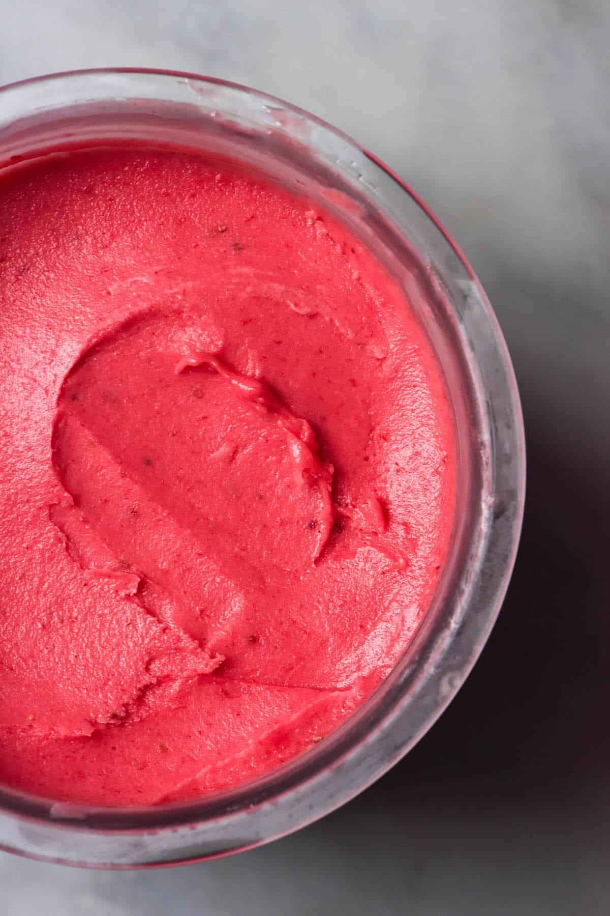 An aerial image of a Ninja Creami tub filled with strawberry ice cream atop a white marble table