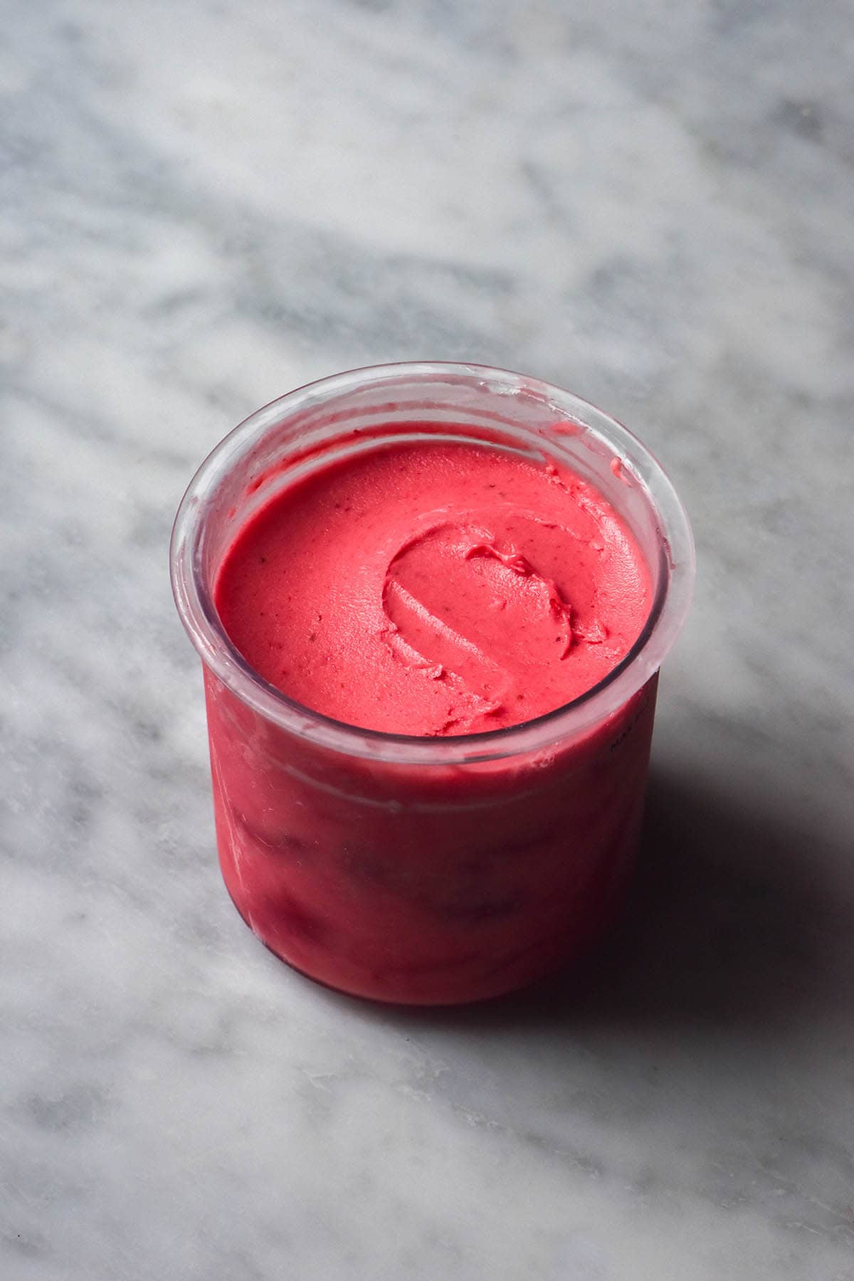 A side on image of a tub of Ninja Creami strawberry ice cream on a white marble table