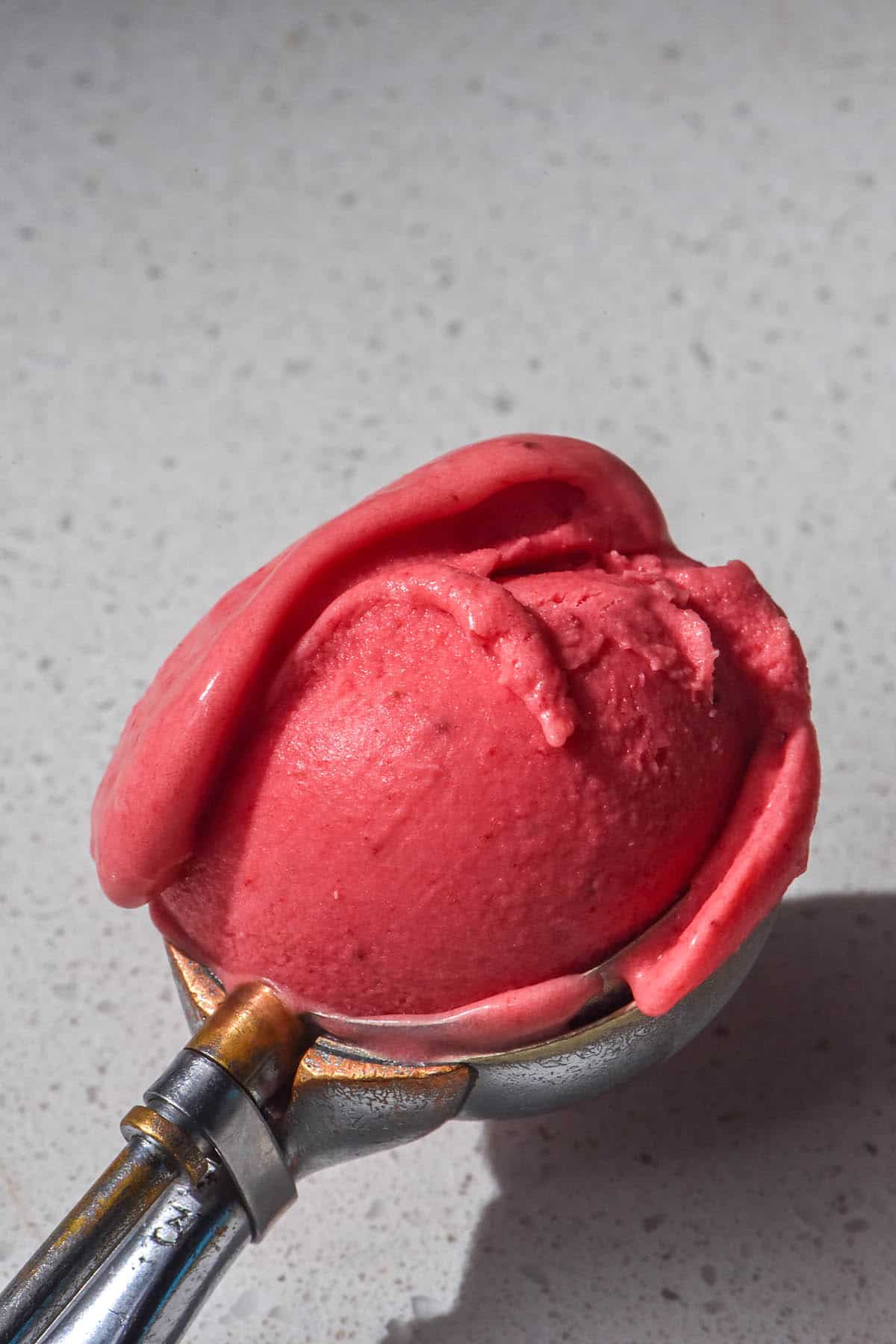 A brightly lit sit on image of a scoop of Ninja Creami strawberry ice cream on a white stone bench top