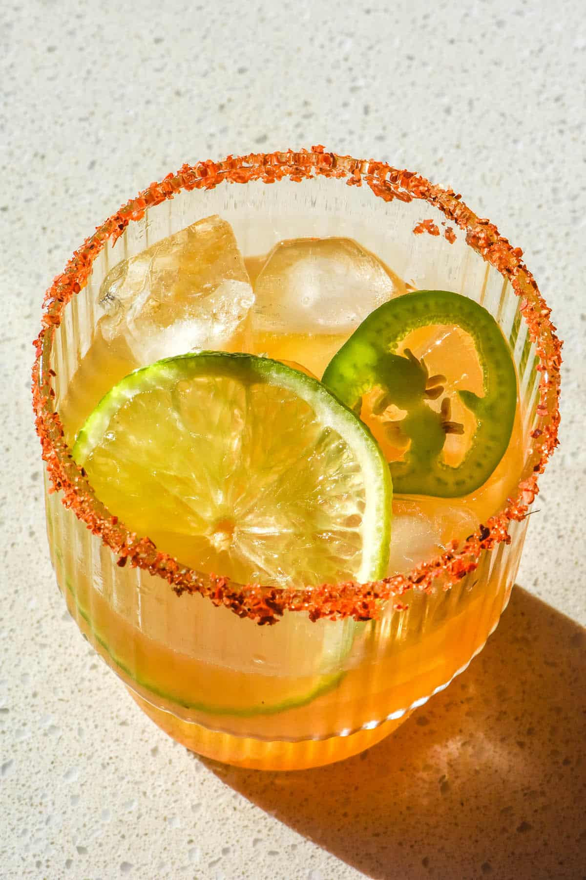 An aerial image of a non alcoholic margarita in bright sunlight on a white stone bench top